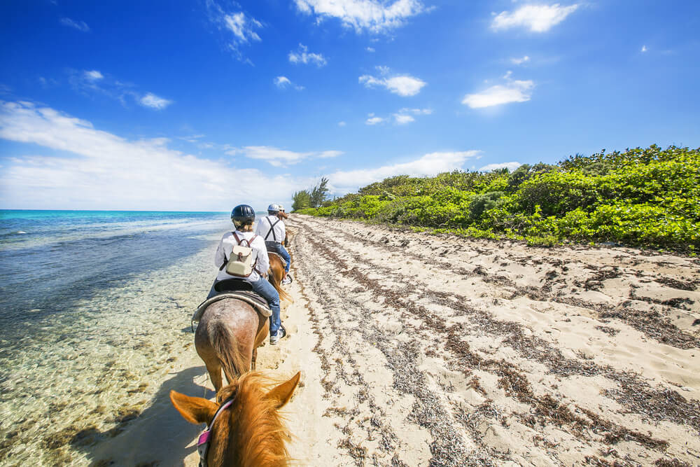 people on horseback wearing helmets on the beach