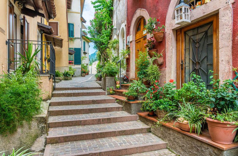 The picturesque town of Gargnano on Lake Garda with bright red, white, blue shutter architecture with tons of plants in terra cotta planters