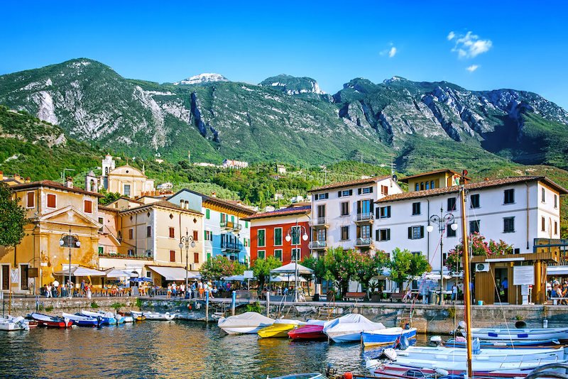 the colorful harbor of the town of malcesine with pastel colored and bright colored houses and boats and mountain backdrop