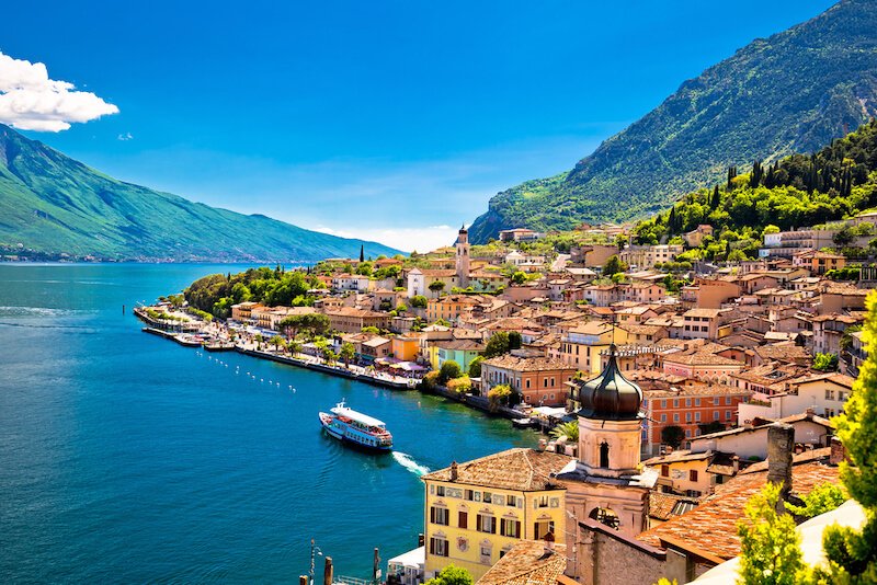 The colorful lakefront town of Limone sul Garda with bright pastel colored architecture on the bright blue lake with one boat taking tourists from town to town on lake garda