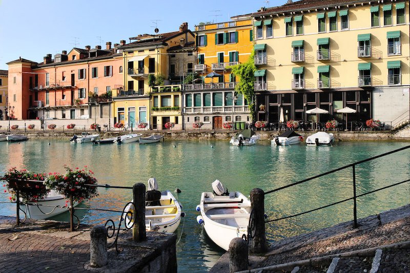 Colorful houses, architecture view with boats and geranium flowers. Little town harbor of Peschiera del Garda, a must-visit on a Lake Garda itinerary