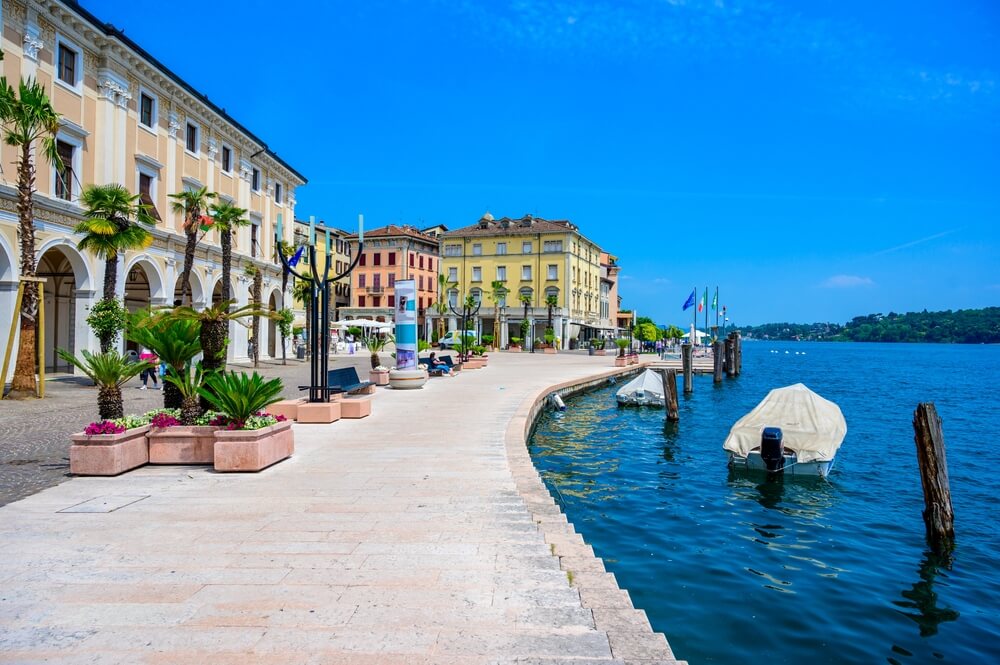 Salò - beautiful village at lake Garda, Italy, lakefront pastel buildings with pale yellow, pale pink, and soft beige facades, palm trees, sunny day