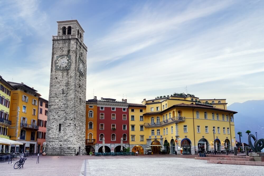 Riva del Garda, Italy. Old town and medieval tower Torre Apponale early in the morning, bright red, yellow, and orange architecture with mountain background