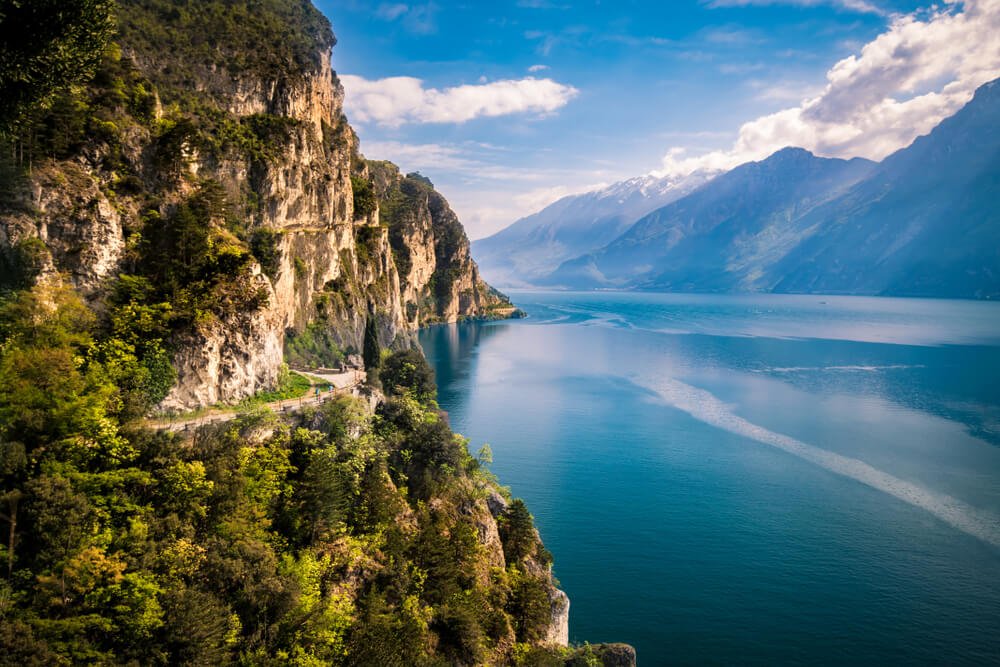 Tranquil lake scenery in Lake Garda, Italy with tree-covered hills and mountains in the distance