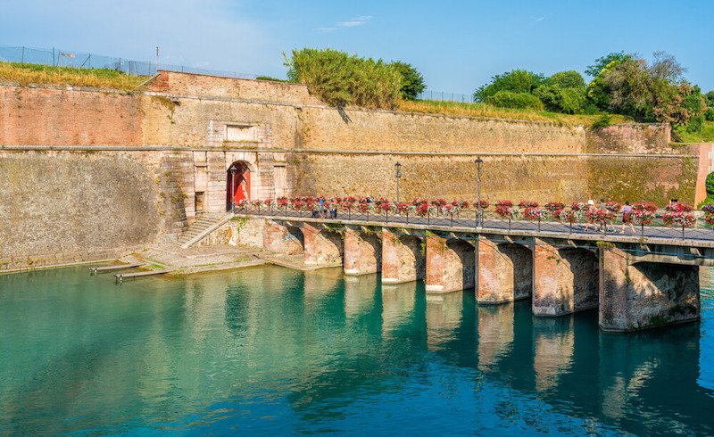 Scenic sight in Peschiera del Garda, village on Lake Garda, with bridge covered in flowers and blue water
