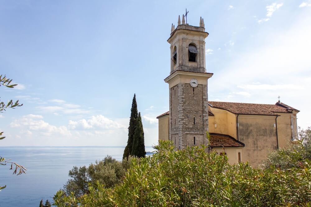 old church with clock on it and belltower and cross on top in the lake garda town 