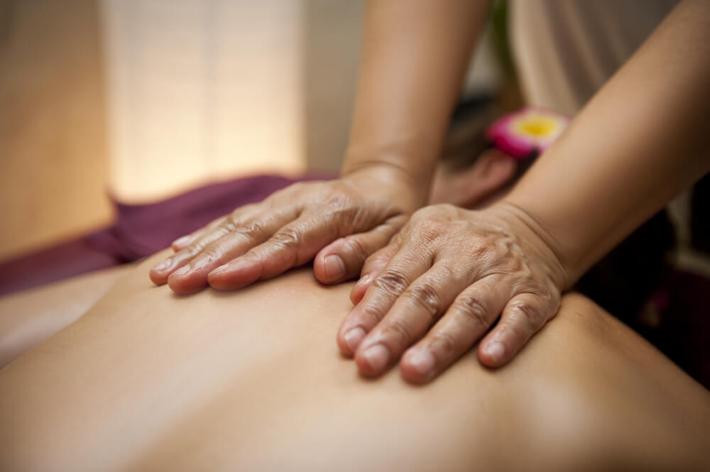 a woman's hands, no nail polish, rubbing someone's back for a massage