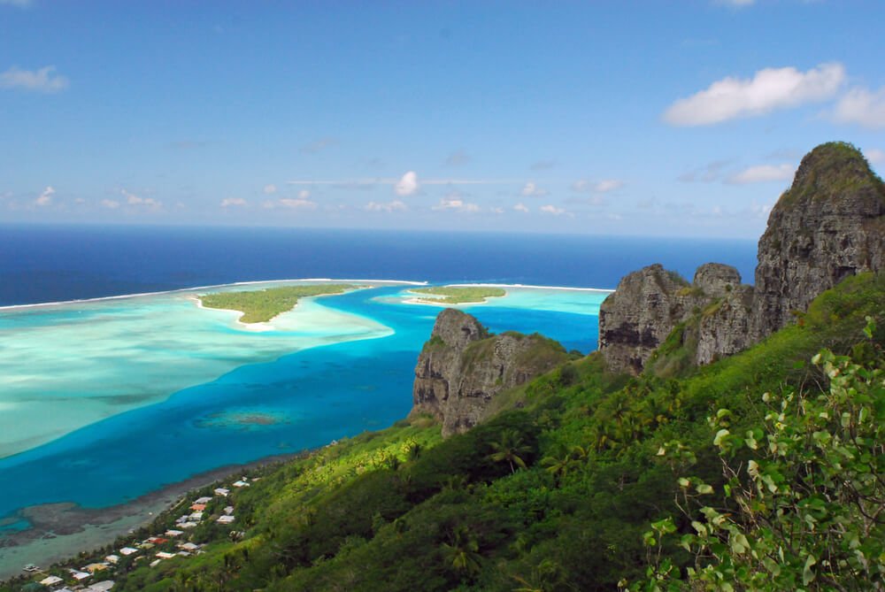 Landscape of Maupiti island showing the mountain top, the lagoon and a small village on a sunny day in French Polynesia