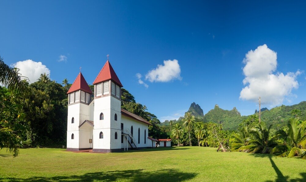 A white church with red roof, two towers, in Moorea tropical landscape on a sunny day