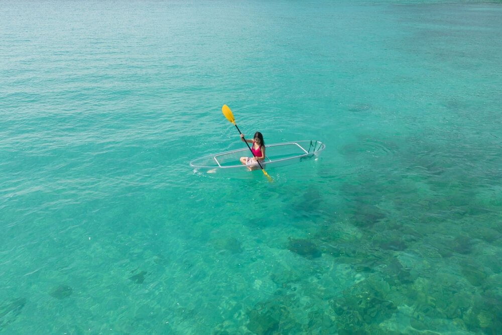 Aerial top view of Asian woman, a tourist, paddling a boat, canoe, kayak or surfboard with clear blue turquoise seawater
