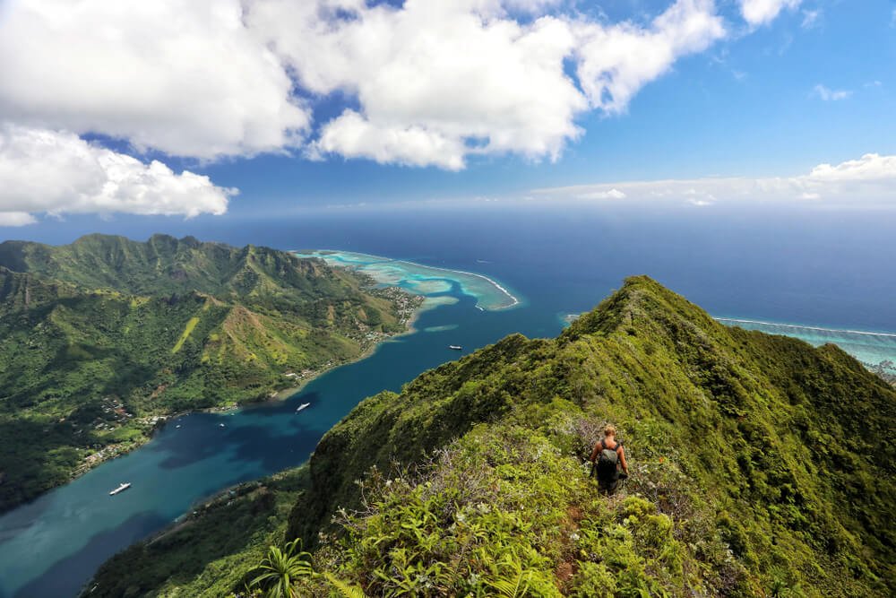 Person hiking on Mount Rotui with views of the Moorea bays below with boats on the water and stunning turquoise waters