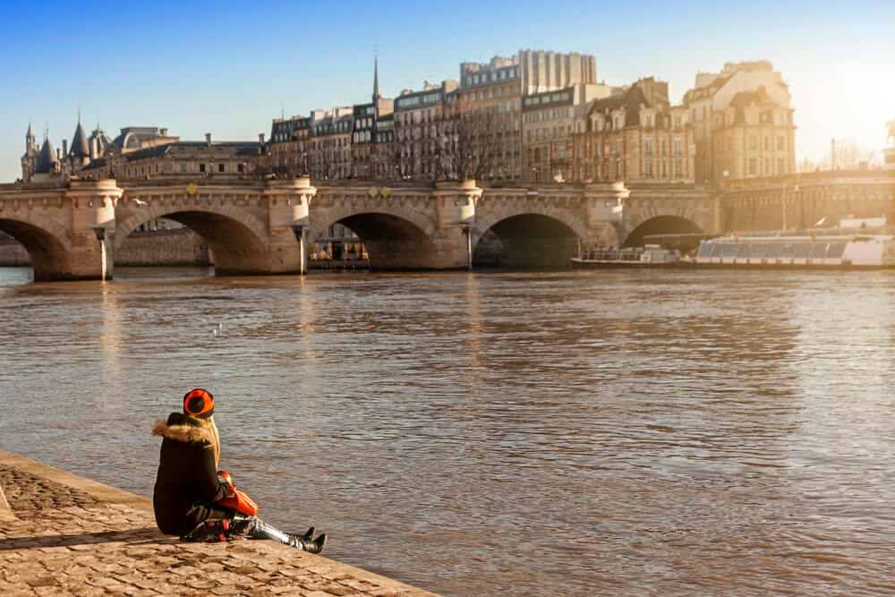Happy tourist woman sitting on the bank of the Seine in Paris in winter.