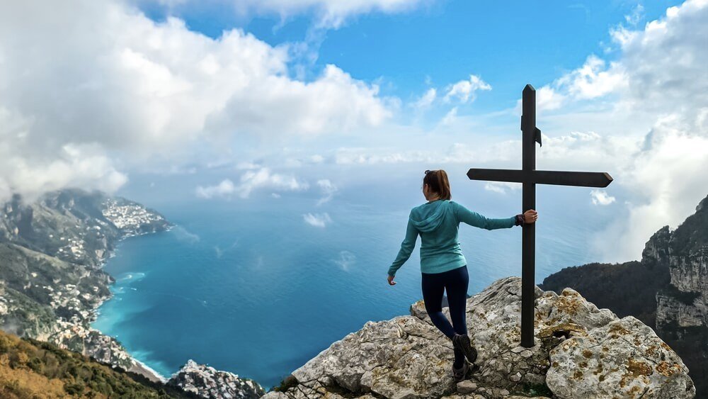 Active woman at summit cross near Santa Maria del Castello. Scenic view on coastal town Positano, Praiano