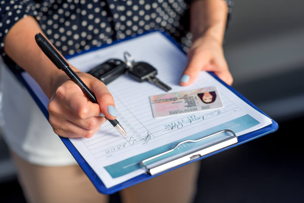 Woman filling out a car rental form and noting any damages on the car before she leaves