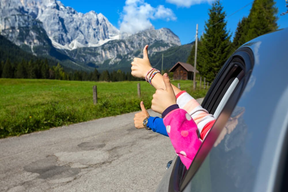Family of three, adult and children, giving a thumbs up while road tripping in Italy