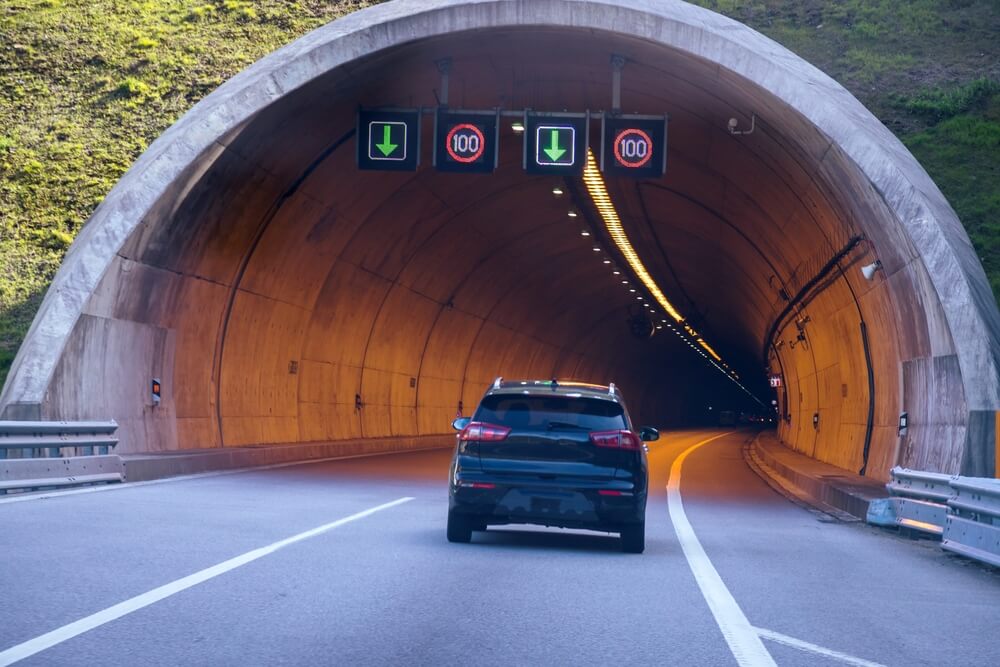 Road signs stating that to drive in the tunnel you must stay under 100 kilometers per hour and a car driving in Portugal.