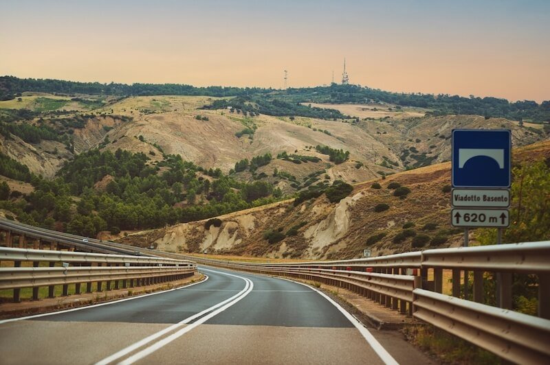 Road trip in Puglia, Italy. Beautiful typical landscape of hills and mountains. Sunset sky. Empty road with nobody.
