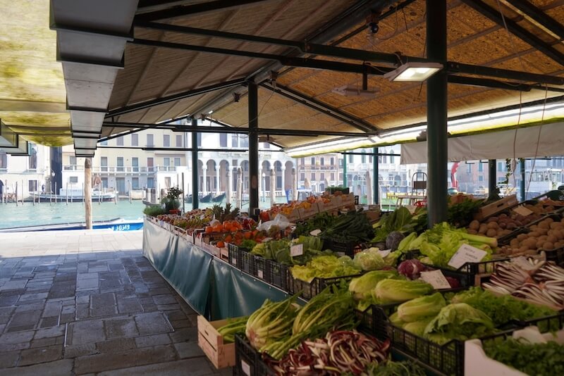 Fruits and vegetables at a stall of the Rialto market in Italy, Venice. In the background the Canal Grande can be seen with some boats and gondolas.