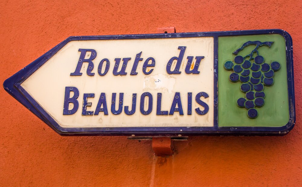 sign that reads route du beaujolais on a red background with grape image