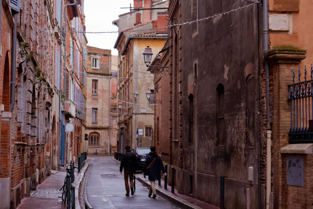 Photo of two people walking in the old part of the city of Toulouse, France during a rainy winter day