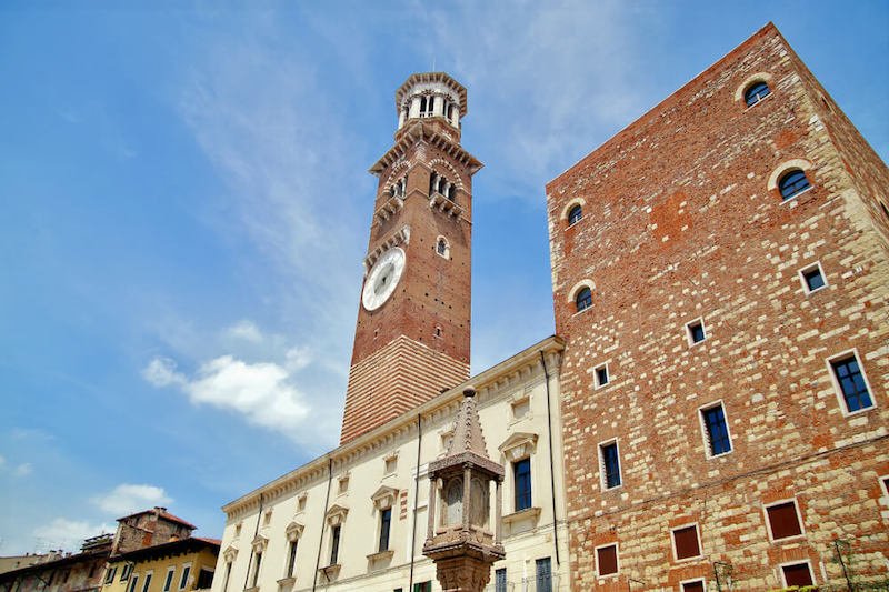 Medieval Lamberti (Torre dei Lamberti) tower XI century with clock, 84 metre and antica ancient column (1400 a.D) on Erbe Square in Verona city. Piazza delle Erbe, - Veneto, Italy