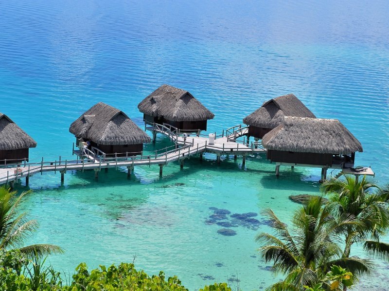 detail of overwater bungalows from above with ombre shades of turquoise to darker blue near the lagoon