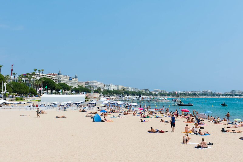 the public beach of cannes with people enjoying the soft sands with cannes city at your back