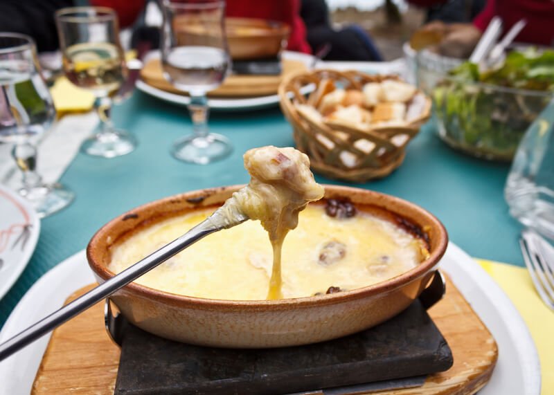 Cheese fondue enjoyed in Switzerland in winter with a metal rod dunking some bread into a pot of melted cheese