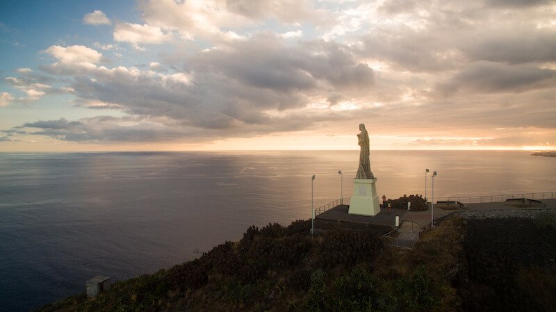 The Christ the King statue is a Catholic monument on Madeira island, seen at sunset, with the large statue against the horizon