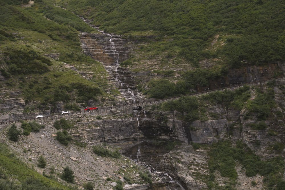 Going To The Sun Road, Glacier National Park, Montana, with red bus leading the way on a mountain road