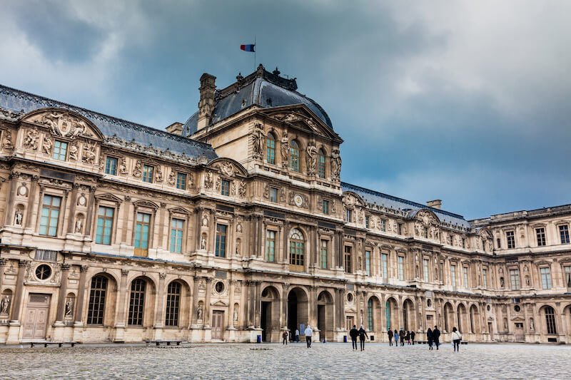 The Louvre in Paris in winter with people in winter outfits for the cold and the palace building looking beautiful on an overcast winter day in Paris