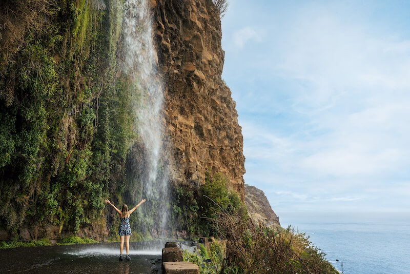 a woman standing underneath a waterfall in madeira island