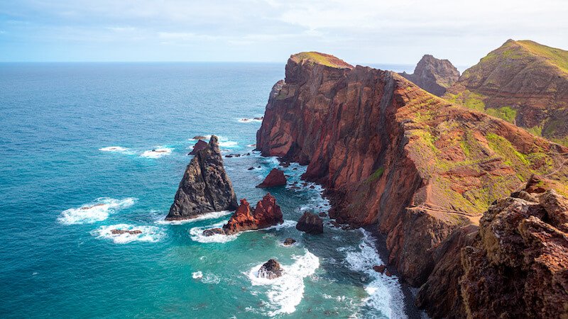 view of sea stacks at the end of the Miradouro de São Lourenço with wild atlantic ocean waves beating against the landscape and creating erosion over time