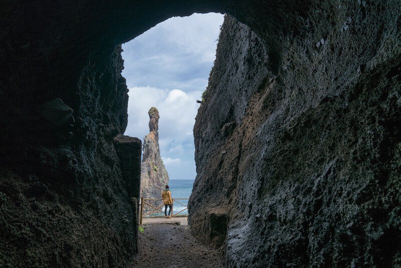 Girl looking at Ribeira da Janela islet between a cave in Madeira, through an arch, looking at the sea