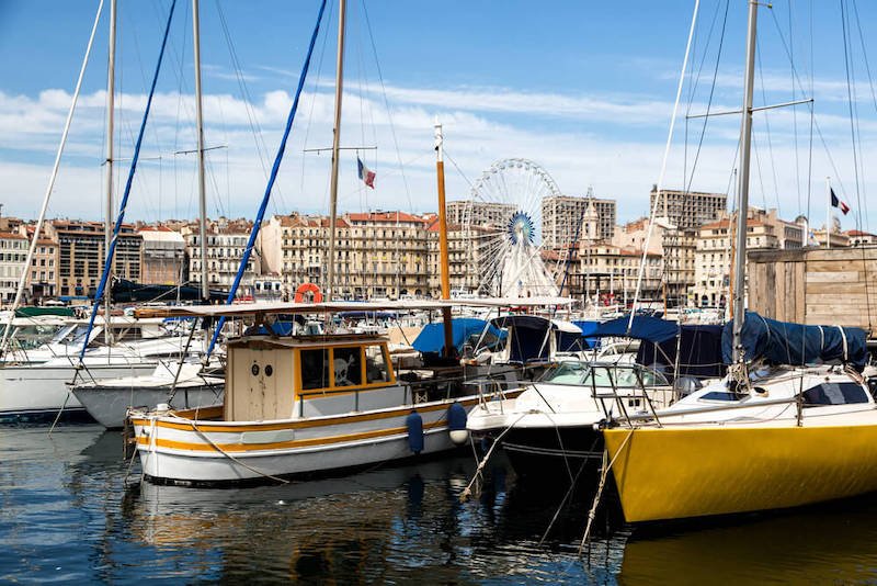 the boats in the harbor of the old port of marseille with a ferris wheel and buildings visible on a sunny day 