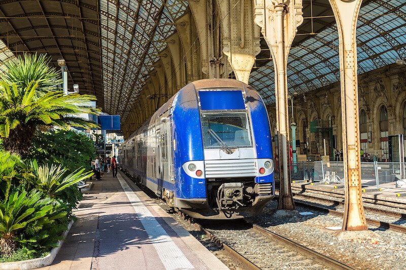 Train station in Nice, with blue train arriving at a train track in the semi open air train terminal