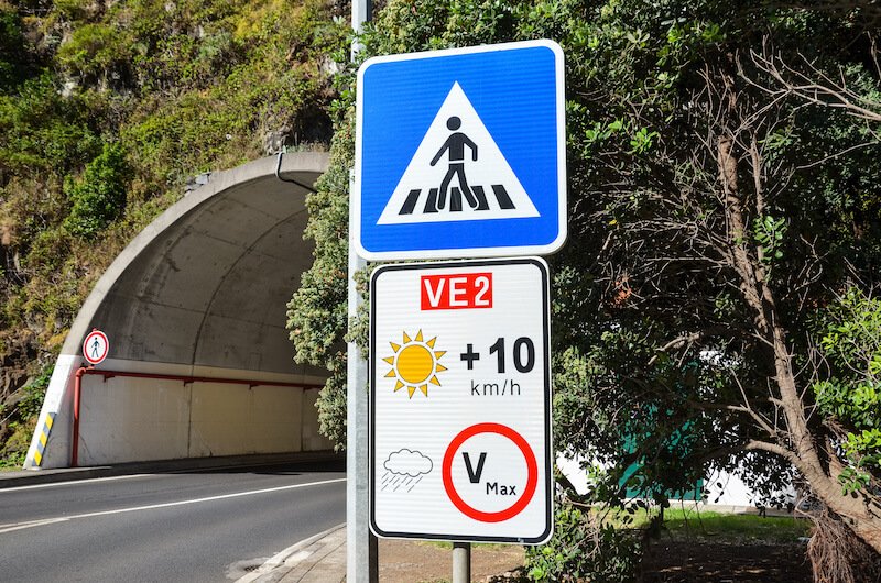 sign about speed limits in maidera, showing a different speed for if its sunny (10 km per hour more) vs. rainy (stay at the max velocity)