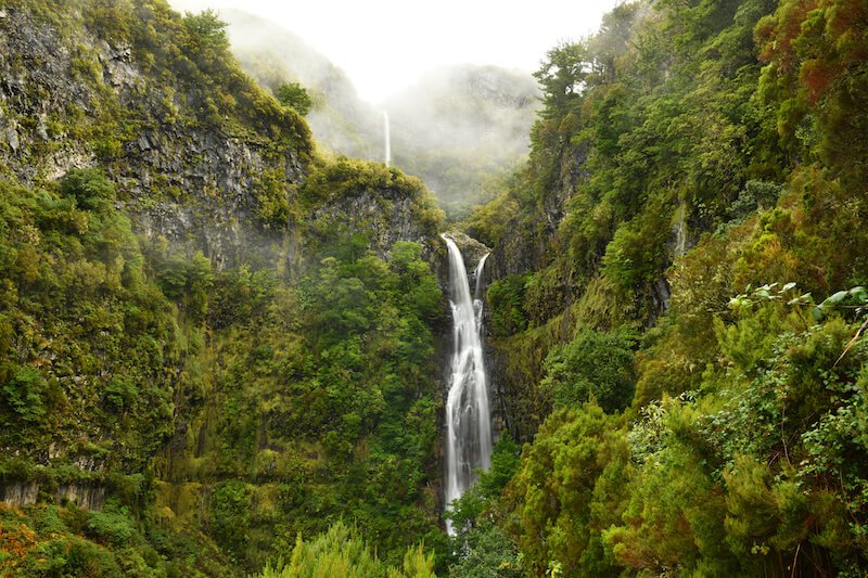 risco waterfall seen from a distance with misty mountains and lush foliage all around the mountains