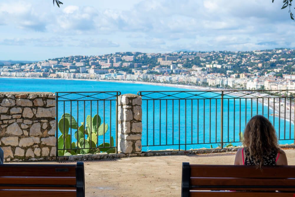 a woman sitting at the viewpoint on castle hill with views over all of nice, with beautiful sand and seaside towns