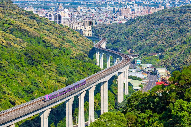 an aerial view of the mrt on an elevated platform making its way through the taiwan landscape on its way to the largest airport on the island