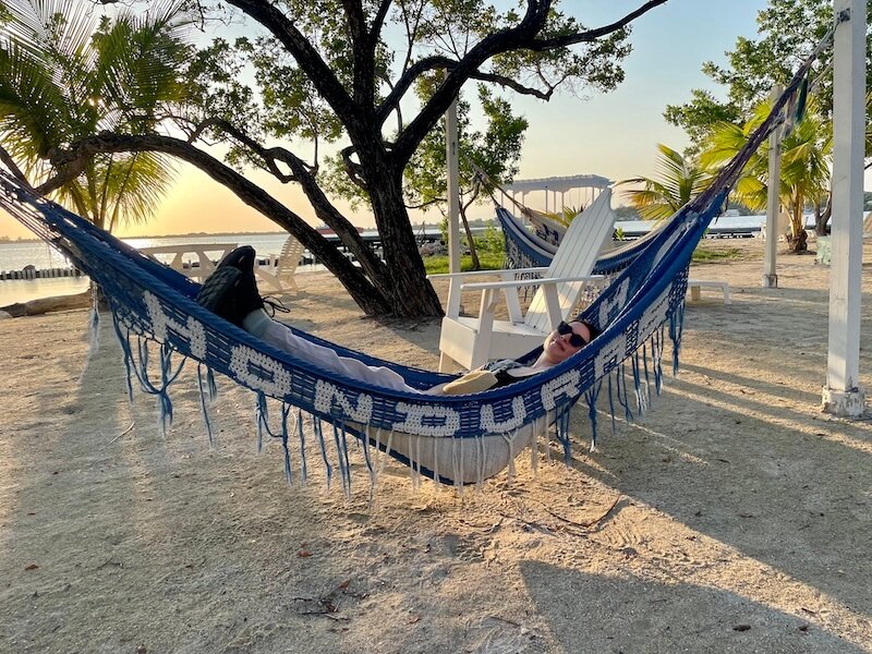 Allison Green relaxing in a hammock that reads "Honduras" in blue and white letters while the sun is setting behind her in Utila