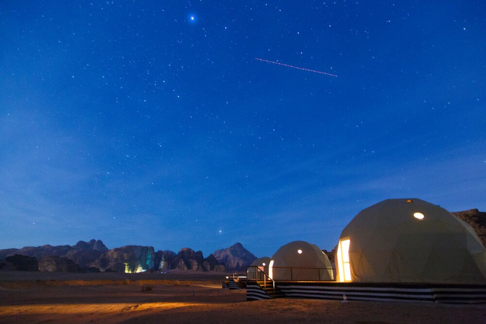 a glamping scene of bubble hotels in jordan at night with lit up tents