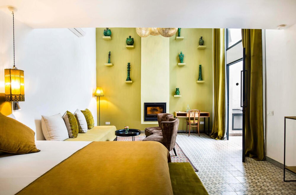 an interior of the riad with a yellow bed, faux fireplace, seating area, work desk, and more