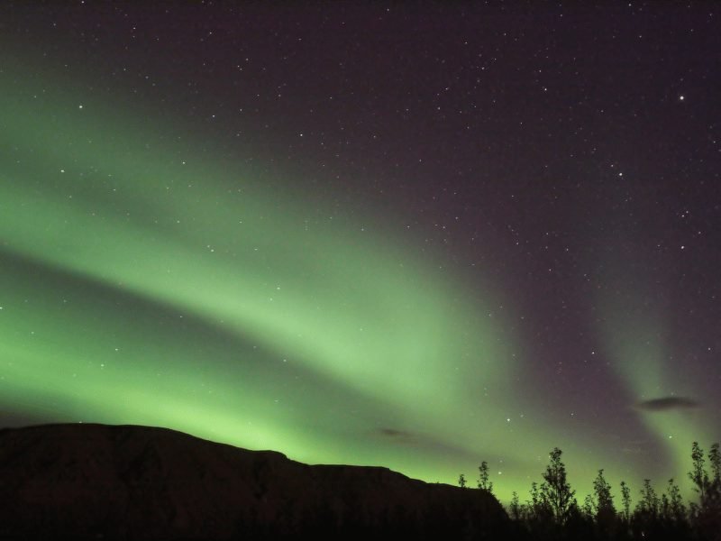 view of the streaky green northern lights over the mountains and landscape