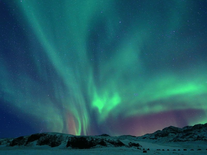 view of the northern lights in the sky with lots of stars and a snowybackdrop at a northern lights hotel in iceland 