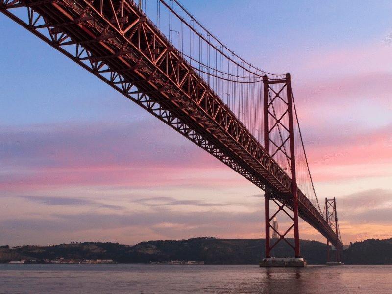 a beautiful red suspension bridge in lisbon that looks quite similar to the golden gate bridge in san francisco, at sunset with a streaky sky