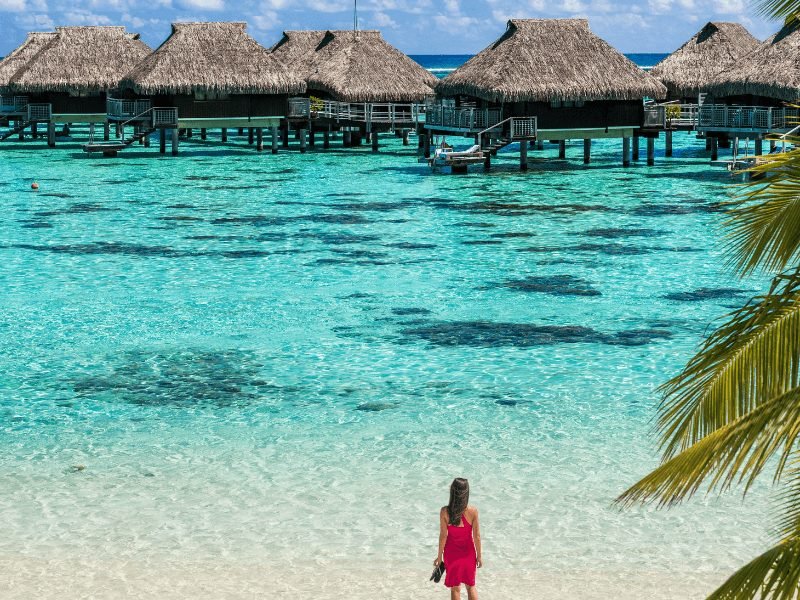 a woman in a red dress standing in front of overwater bungalows in moorea