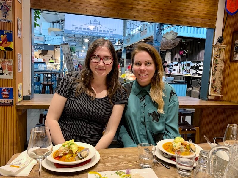 Allison Green and Megan starr at a food hall in Tampere, eating a fish stew for lunch and having a glass of wine