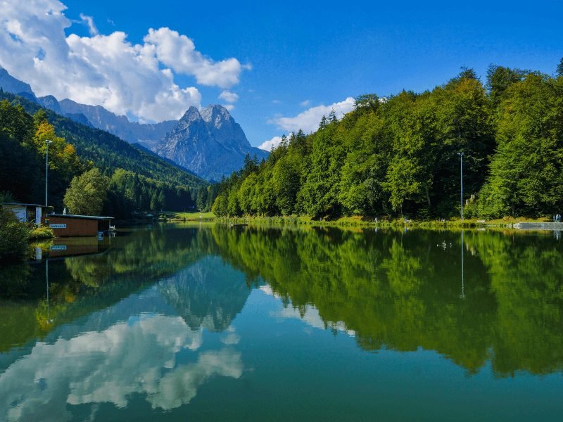 Riessersee with clear reflection of trees and mountains and clouds in the still waters