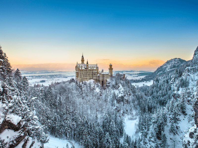 Winter scene of a snow-covered Neuschwanstein Castle at sunset with mist and snowy landscape